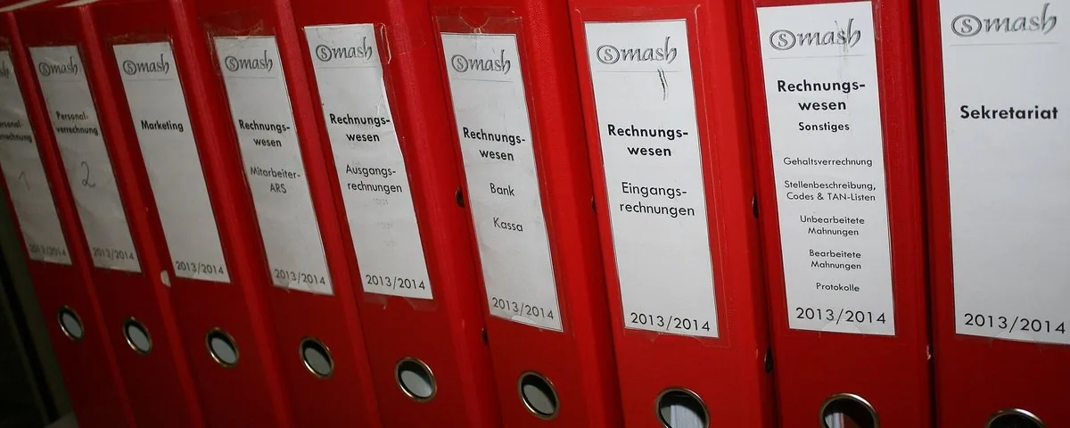 A row of red lever-arch files with typed spine labels